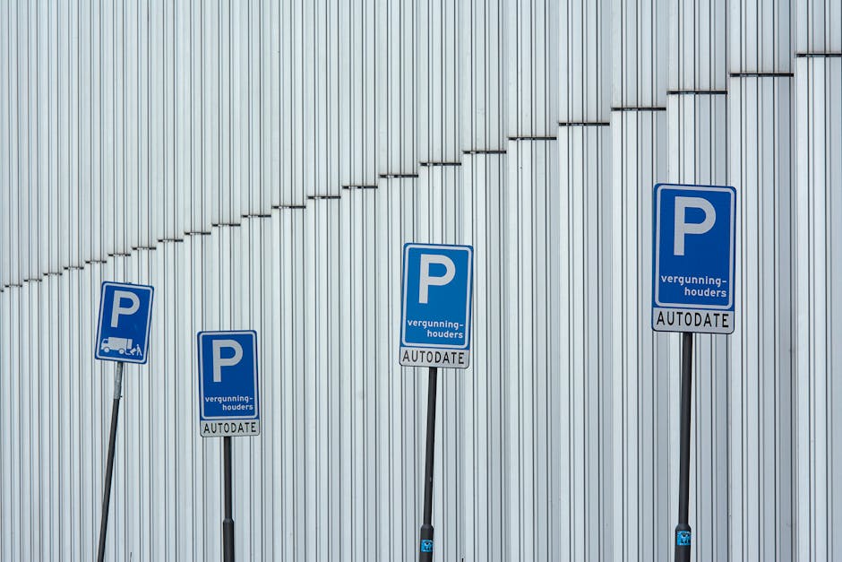 Four blue parking permit signs are mounted on flexible metal posts in front of a modern building with a silver, vertically ribbed metal facade. The signs display a large white 'P' indicating parking, with supplementary text in Dutch, including the words 'vergunning-houders' and 'AUTODATE.' The signs are aligned from left to right, with the posts slightly curved and varying in height. The background shows the building's smooth, metallic surface, with subtle horizontal lines and diagonal shadows created by surrounding lighting. This image illustrates designated parking areas for authorized vehicles, relevant to house removals and moving services, such as those offered by Ilford Man and Van, especially within regulated parking zones like the Redbridge council area.