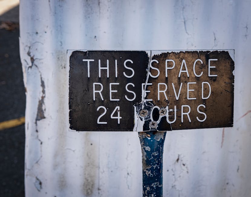 Four blue parking permit signs are mounted on flexible metal posts in front of a modern building with a silver, vertically ribbed metal facade. The signs display a large white 'P' indicating parking, with supplementary text in Dutch, including the words 'vergunning-houders' and 'AUTODATE.' The signs are aligned from left to right, with the posts slightly curved and varying in height. The background shows the building's smooth, metallic surface, with subtle horizontal lines and diagonal shadows created by surrounding lighting. This image illustrates designated parking areas for authorized vehicles, relevant to house removals and moving services, such as those offered by Ilford Man and Van, especially within regulated parking zones like the Redbridge council area.
